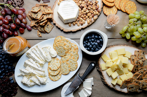 A table with fresh grapes, blueberries, brie, crackers, and honey, spread out for a party.
