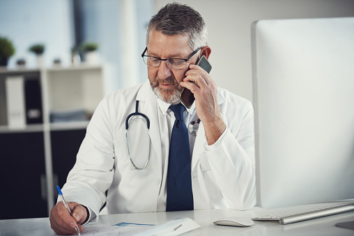 Shot of a mature doctor using a mobile phone at a desk in his office