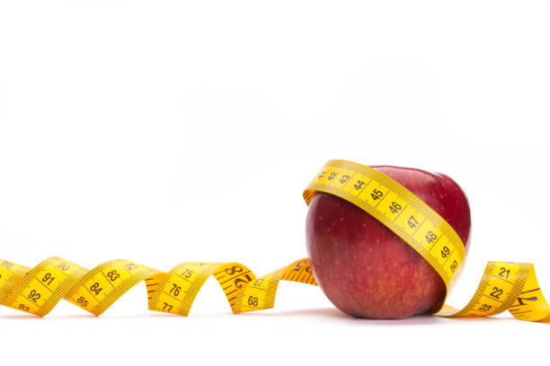 fita amarela medida em torno de uma maçã vermelha como um conceito de perda de peso - tape measure apple dieting measuring - fotografias e filmes do acervo