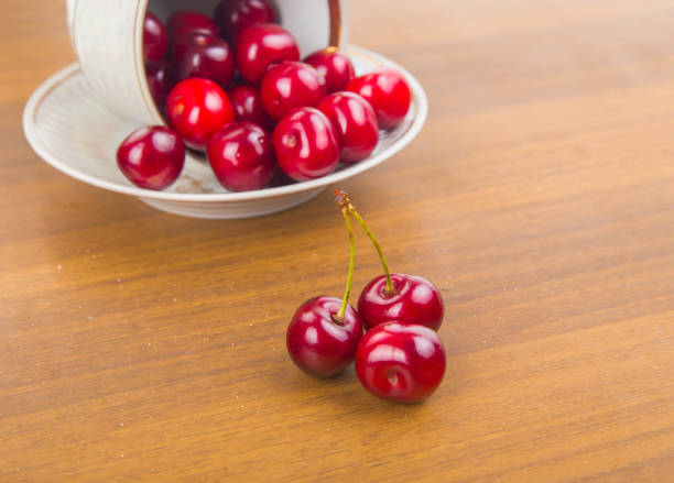 istock Sweet cherries in a white cup on a wooden table with two cherrie 875847636