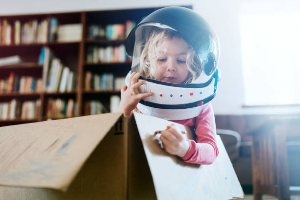 Children Imagine Space Adventure in Cardboard Box A boy and girl at home in their living room play in and color a cardboard box, one of them wearing a toy astronaut helmet.  Imagination, discovery, and fun. girls playing stock pictures, royalty-free photos & images