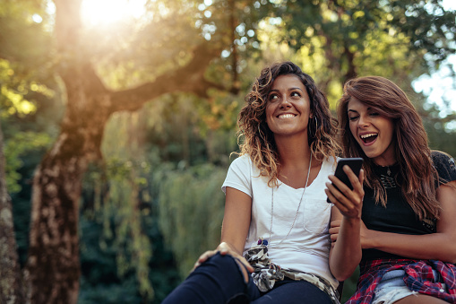 Two young girls sitting in a park looking at a mobile phone