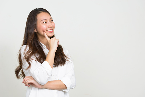 Studio shot of young beautiful Asian woman wearing white shirt against white background