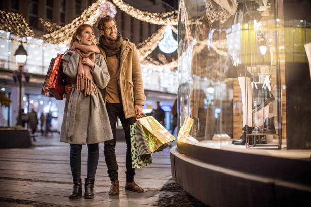 Christmas joy of shopping Young couple walking in shopping mall for Christmas. Holding Christmas gifts and wearing warm clothing. window shopping at night stock pictures, royalty-free photos & images