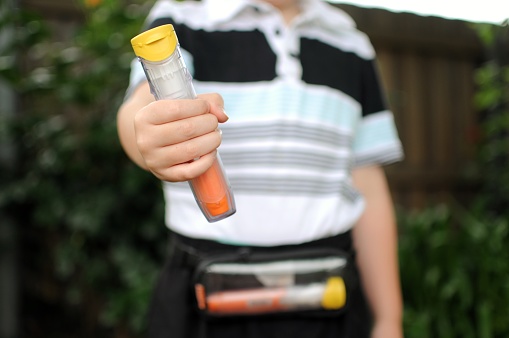 Child holding a anaphylaxis Auto injector with one also in small pouch. Carry case is being worn by a child.