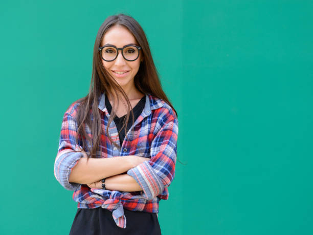 Young beautiful woman wearing checkered shirt against blue painted wall Studio shot of young beautiful woman wearing checkered shirt against blue painted wall horn rimmed glasses stock pictures, royalty-free photos & images