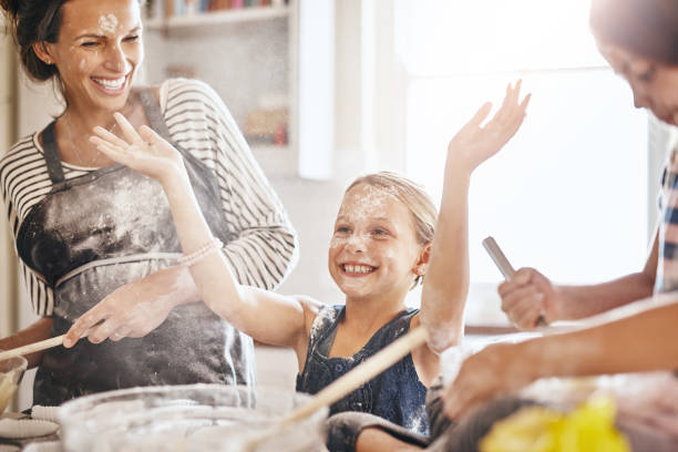 It's not flour, it's fairy dust! Shot of two little girls having fun while baking with their mother in the kitchen flour mess stock pictures, royalty-free photos & images