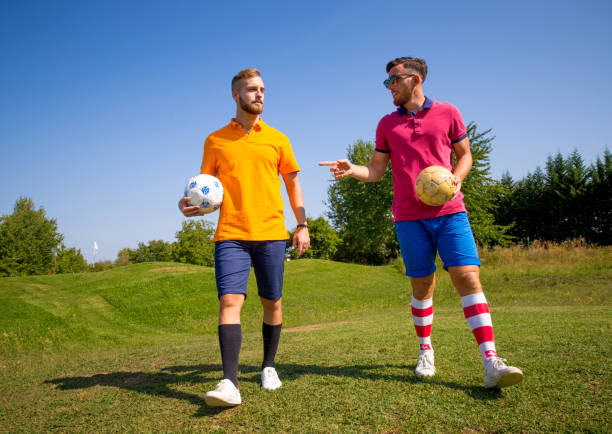 istock Two Young Adults Walking on Golf Course Holding Soccer Ball 875952150