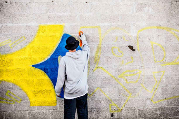 Late Teen Graffiti Artist Drawing Graffiti on Wall.
