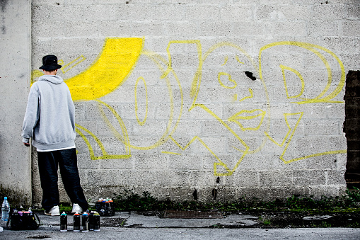 Late Teen Graffiti Artist Drawing Graffiti on Wall.