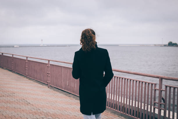 istock Slender young woman in a black coat walks 875961636