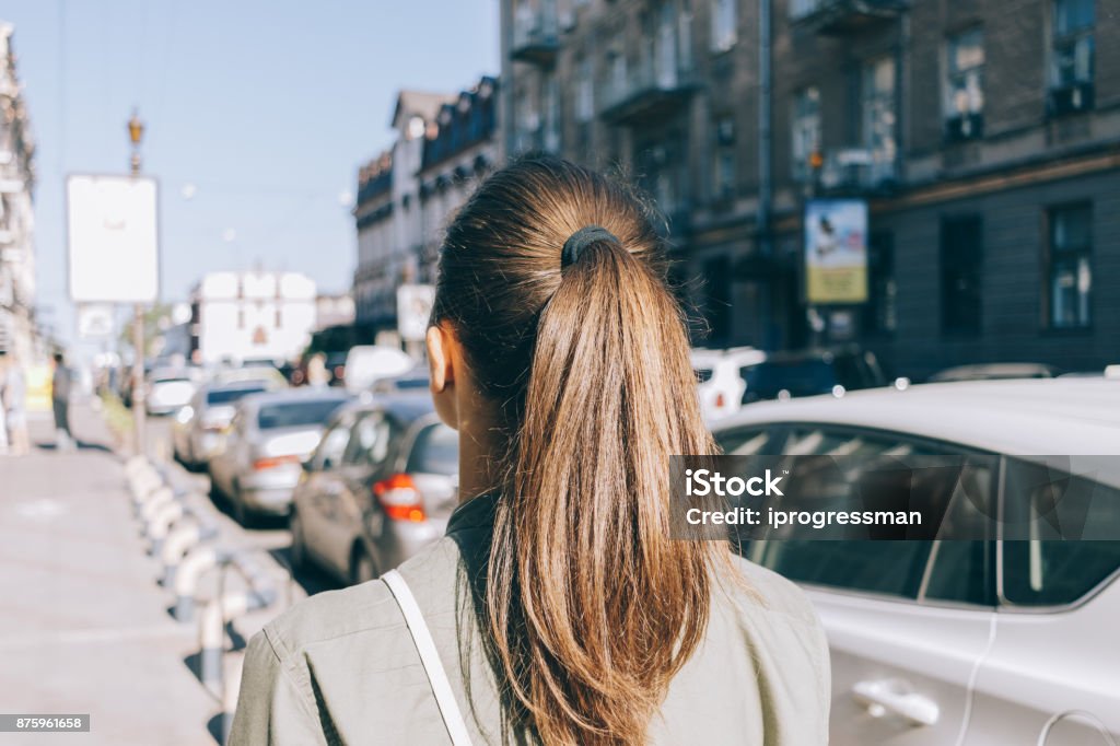 View from the back of a girl with brown hair View from the back of a girl with brown hair walking through the city in summer Ponytail Stock Photo