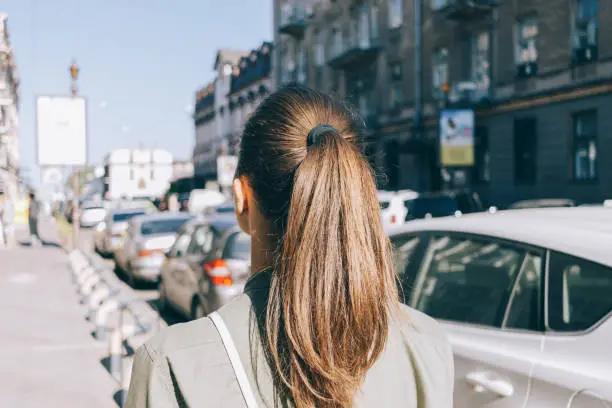 View from the back of a girl with brown hair walking through the city in summer