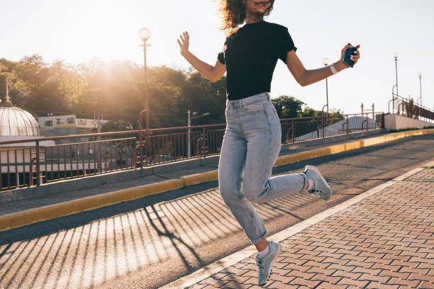 Happy girl with curly brown hair jumping in the city Happy girl with curly brown hair jumping in the city in summer acrobatic activity photos stock pictures, royalty-free photos & images