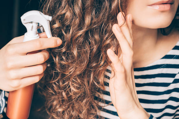 donna che applica spray sui capelli castani ricci - cura dei capelli foto e immagini stock