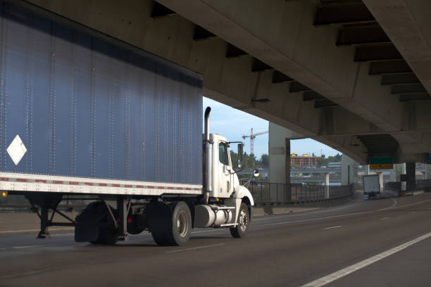 istock Big rig semi truck with day cab and covered tarp semi trailer going under overpass bridge 875965420
