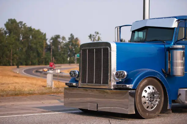 Photo of Classic blue big rig semi truck with chrome accessories running on the road