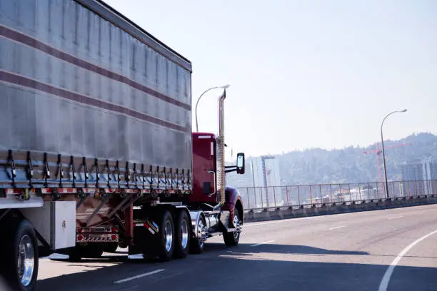 Photo of Red big rig day cab semi truck with covered trailer turning on overpass city road