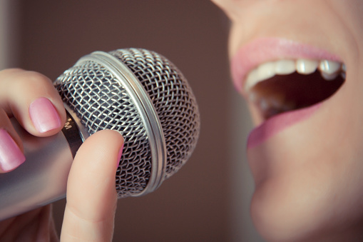 A woman sings into a microphone at a recording studio, her mouth close up