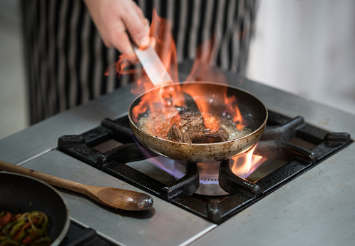 Close up of unrecognizable chef using a frying pan to flambe a steak at a restaurant