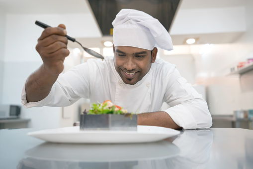 Indian chef adding vinaigrette to a salad ready to serve and looking very happy