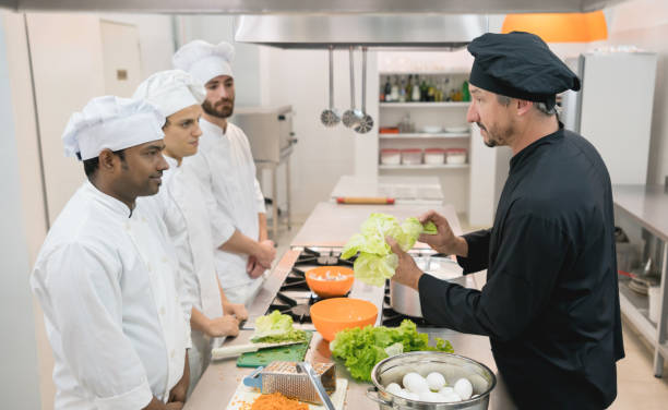 koch-lehrer zeigen einen frischen salat zu seinen schülern und alle aufmerksamkeit - restaurant chef gourmet dining stock-fotos und bilder