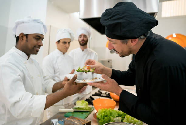 Head chef checking a salad that the sous chef just made and all of the team paying attention to his feedback