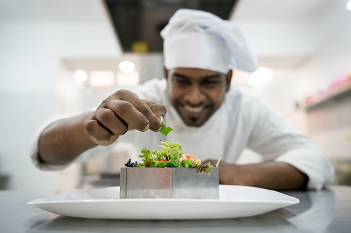 Cheerful indian chef making a salad to serve as appetizer at a restaurant - Focus on foreground