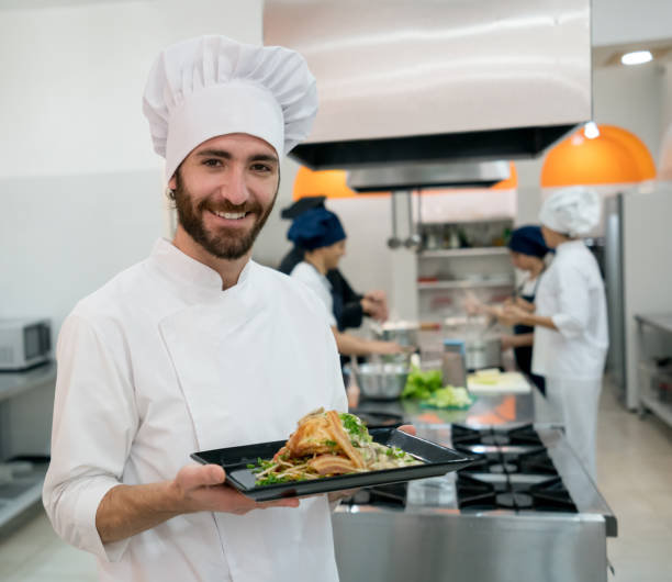istock Proud chef holding a dish he just prepared while his team is working at the background 875992408