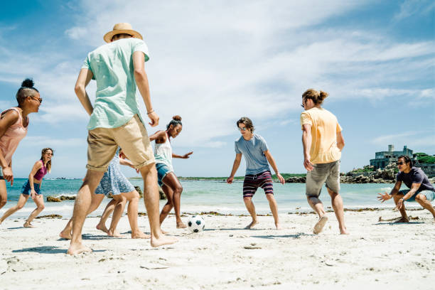 amigos jugando al fútbol en la playa en día soleado - beach football fotografías e imágenes de stock