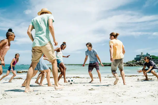 Photo of Friends playing soccer at beach on sunny day