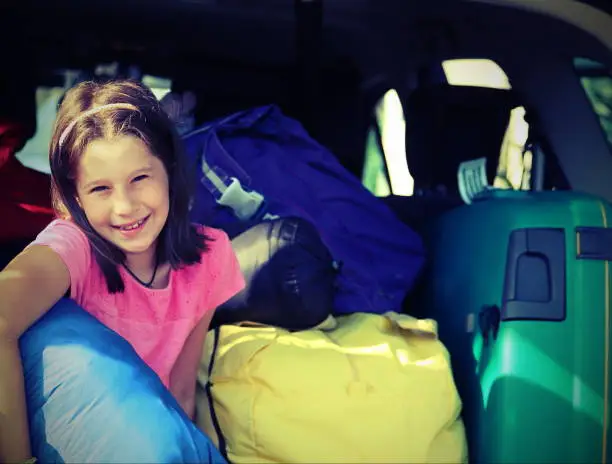 Photo of Pretty little girl fills the suitcases on the car  with vintage