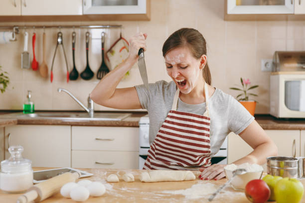 istock A young evil and aggressive woman sitting at a table and attacking the dough with a knife in the kitchen. Cooking home. Prepare food. 876007620