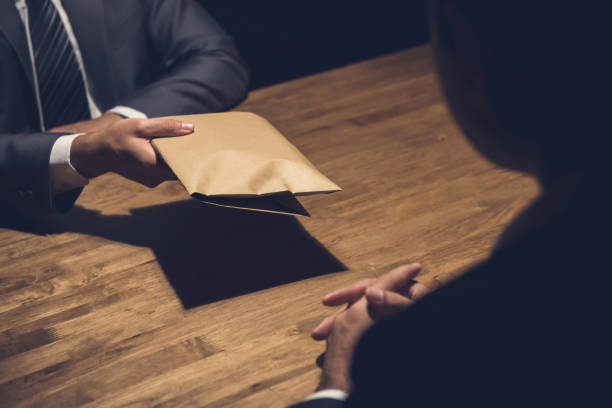 istock A man giving bribe money in a brown envelope to another businessman 876018768