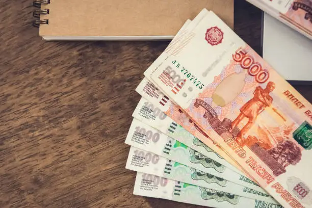 Photo of Russian Ruble money banknotes on a wooden desk with a notebook.