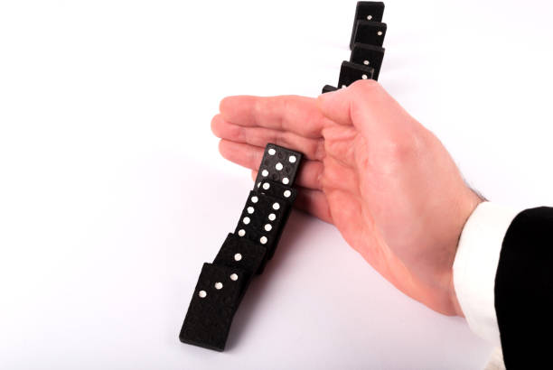 Businessman hand stopping dominoes row from falling on white table, close up