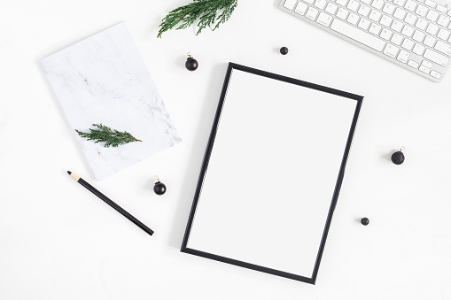 Christmas desk. Black frame, keyboard, marble notebook and christmas tree branches on white background. Flat lay, top view, copy space