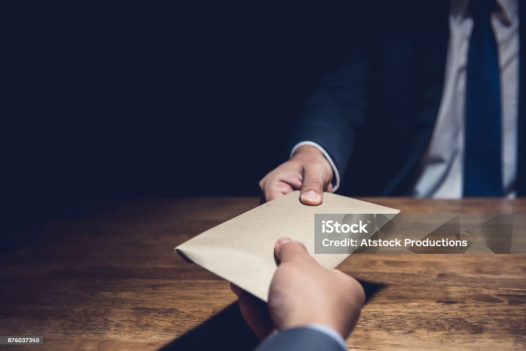 A man giving bribe money in a brown envelope to another businessman in the dark A man giving bribe money in a brown envelope to another businessman in a corruption scam Corruption Stock Photo