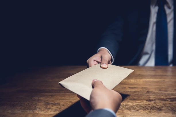 A man giving bribe money in a brown envelope to another businessman in the dark A man giving bribe money in a brown envelope to another businessman in a corruption scam corruption stock pictures, royalty-free photos & images