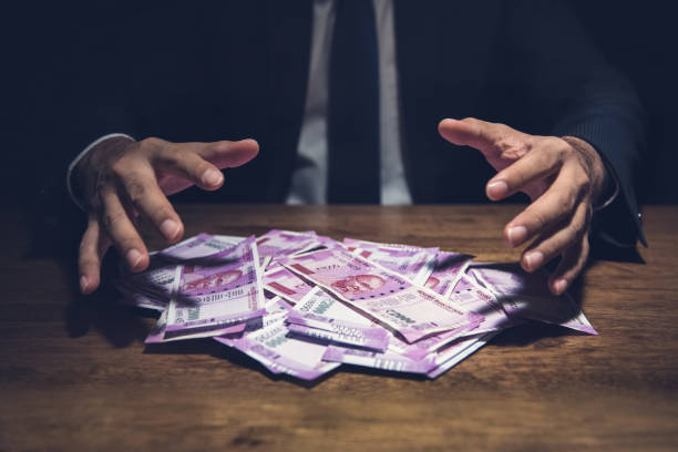 Businessman taking pile of money, Indian Rupee banknotes, on his desk in a dark office. Businessman taking pile of money, Indian Rupee banknotes, on his desk in a dark office  - corruption concept elasmobranch stock pictures, royalty-free photos & images