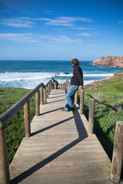 istock man croouching on wooden pathway observing waves with binoculars on surf spot amado beach, algarve, portugal 876037994