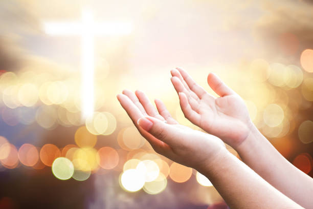 Prayer hands of a young girl on background of candle light and colorful Christmas bokeh lights. Person praying alone in silent concept.