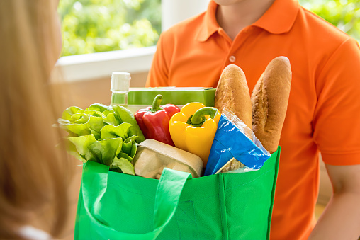 Grocery store delivey man wearing orange polo-shirt delivering food to a woman at home