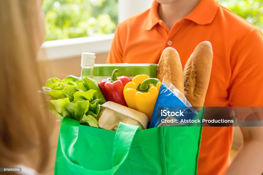 Grocery store delivey man  delivering food to a woman at home Grocery store delivey man wearing orange polo-shirt delivering food to a woman at home Delivering Stock Photo