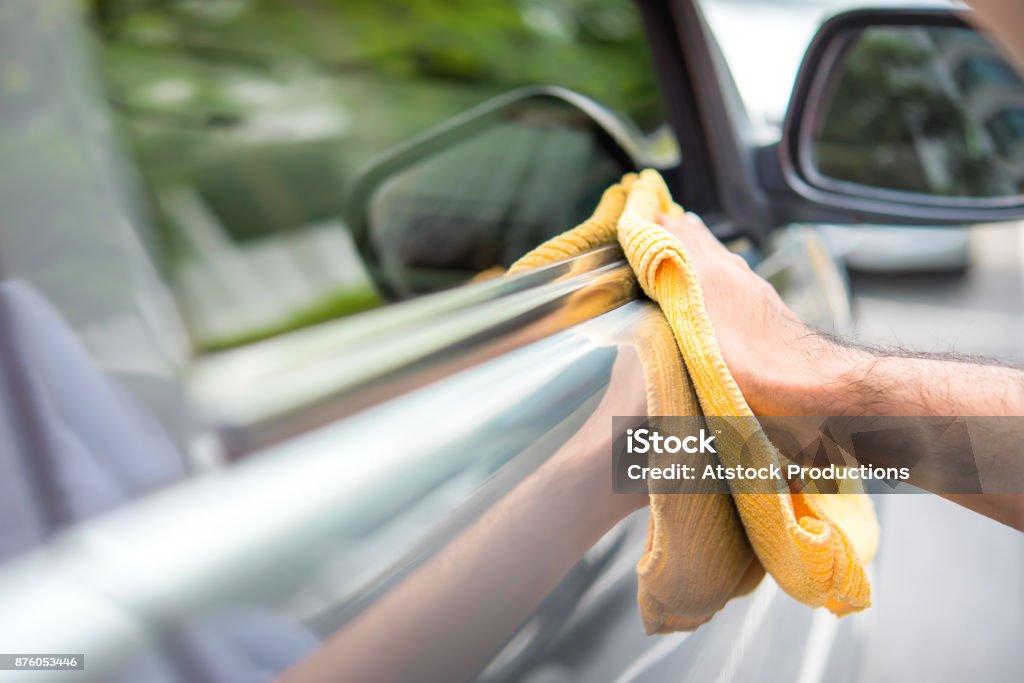 Un uomo che pulisce un'auto con panno giallo in microfibra - dettagli dell'auto, vale e concetto di servizio automatico - Foto stock royalty-free di Automobile