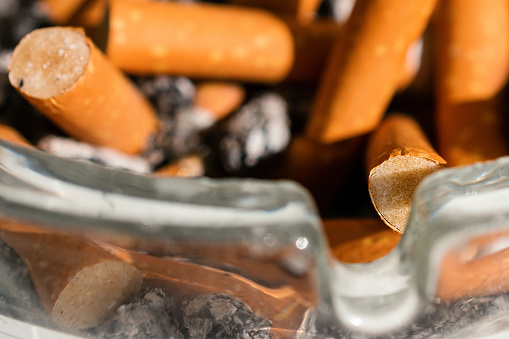 A close-up shot of cigarette butts with orange filters in a glass ashtray.