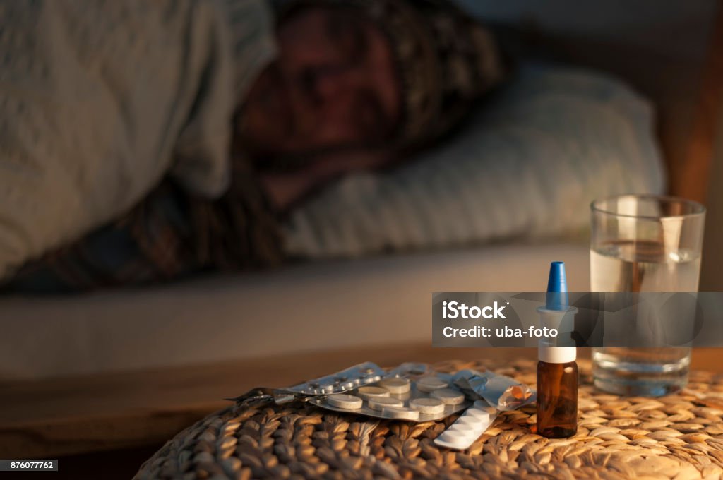 A man lie with cold in your bed A man lying with cold in bed lying in front of him medicines, selective focus. Nasal Spray Stock Photo