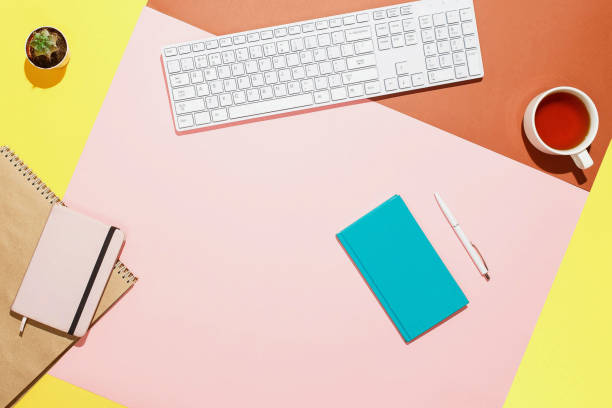 istock Modern home office workspace. Flat lay composition of keyboard, cactus, diary, notebook with pen and cup of tea on colorful desk. Pink, yellow, aquamarine and and brown colours 876097670