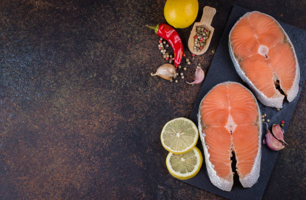 istock Two fresh raw salmon steaks on slate board with salt, peppers, lemon on dark table background, top view. Healthy Dieting Food Concept 876108842