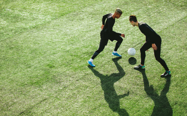 Soccer players in action on field Top view of two teenagers playing football during team practice in field. Young soccer players playing on the sports grass field. softball pitcher stock pictures, royalty-free photos & images